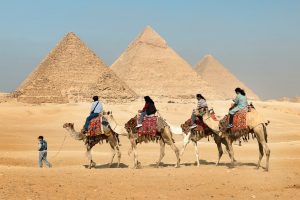 four people riding on camels across the pyramids